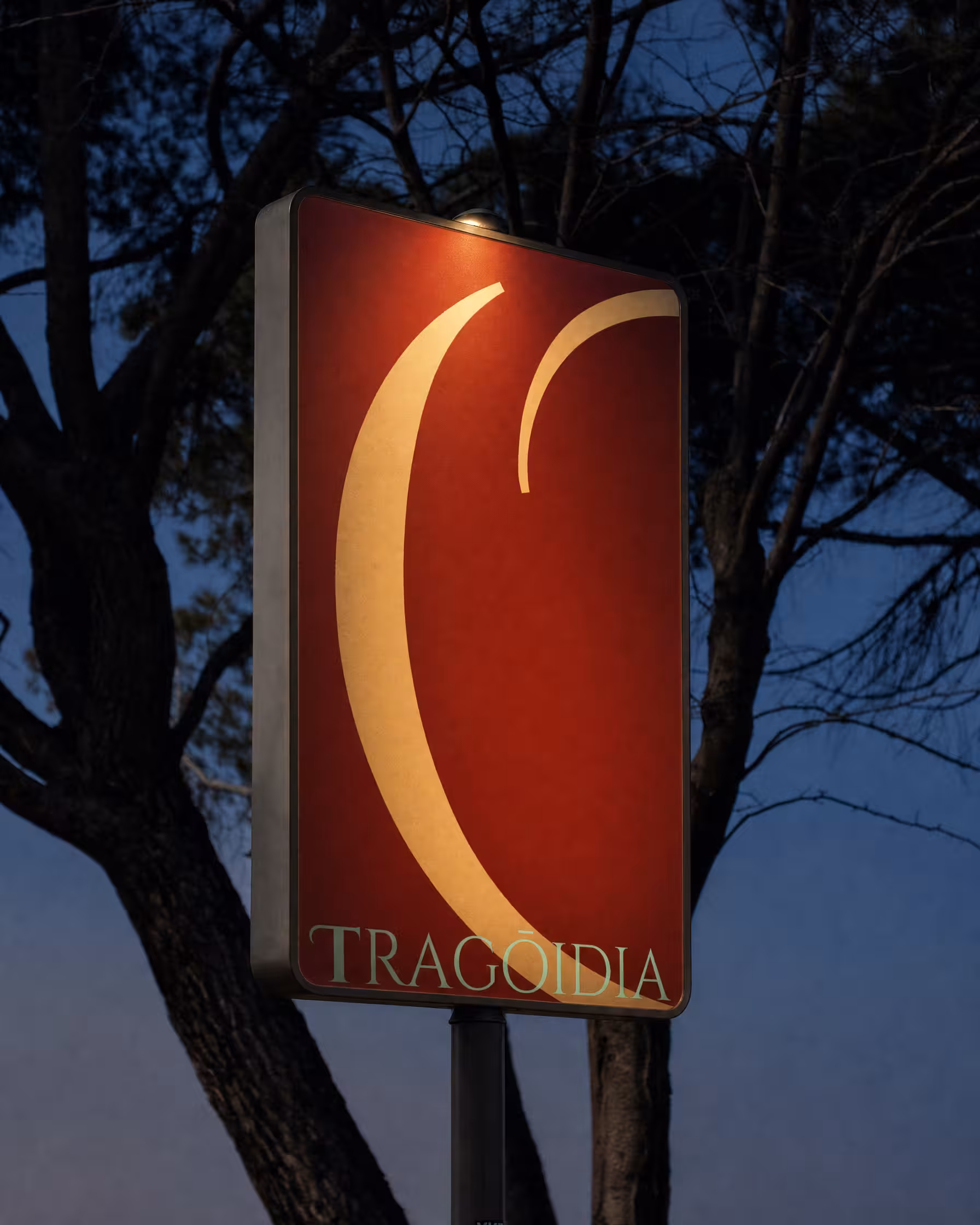 Tragoidia branding mockup on an illuminated outdoor sign at dusk